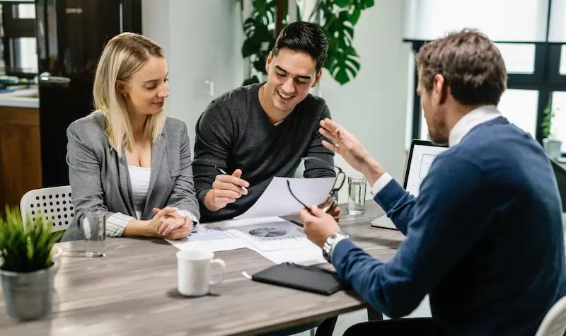 young happy couple reading terms mortgage documents while having meeting with real estate agent home focus is young man
